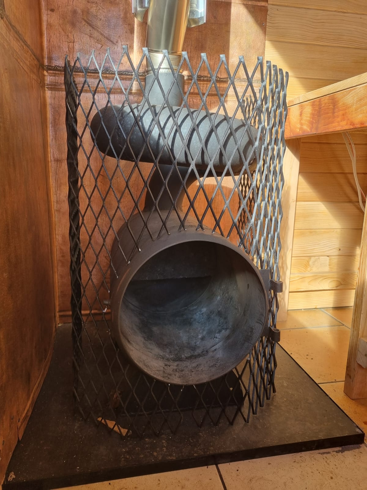 A dark metal fireplace  enclosed in a black diamond-pattern metal guard mesh, set against a wood-paneled background.
