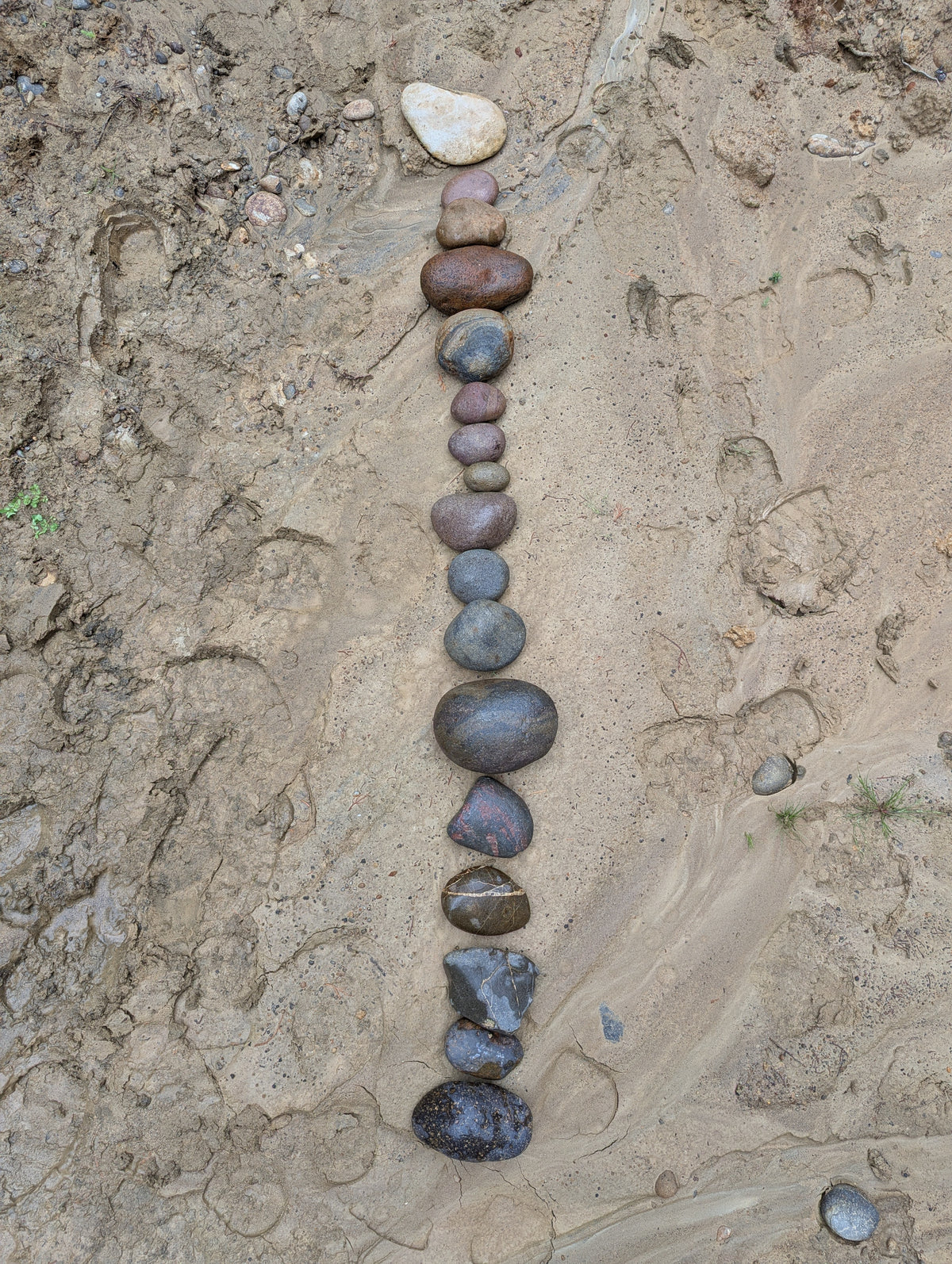 A vertical line of smooth river stones arranged on sandy ground.